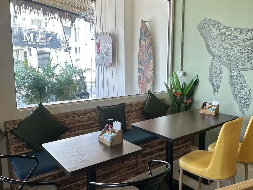 Cozy indoor seating area at Wilson’s Cafe Phuket Town with wooden tables and window view